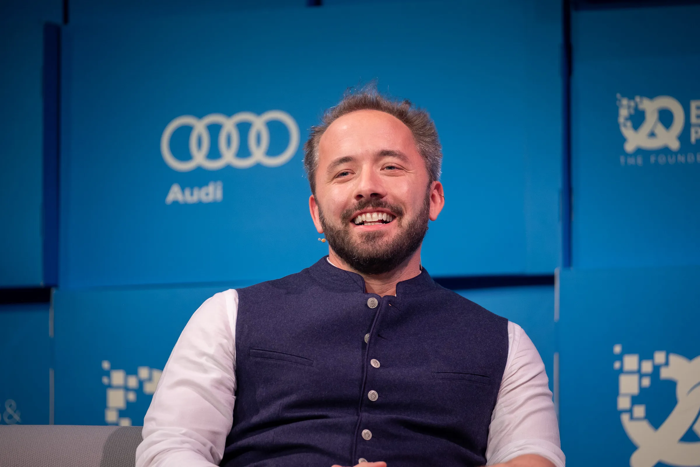 Bits & Pretzels 2019 - Speaker laughing on stage, Audi sponsor backdrop