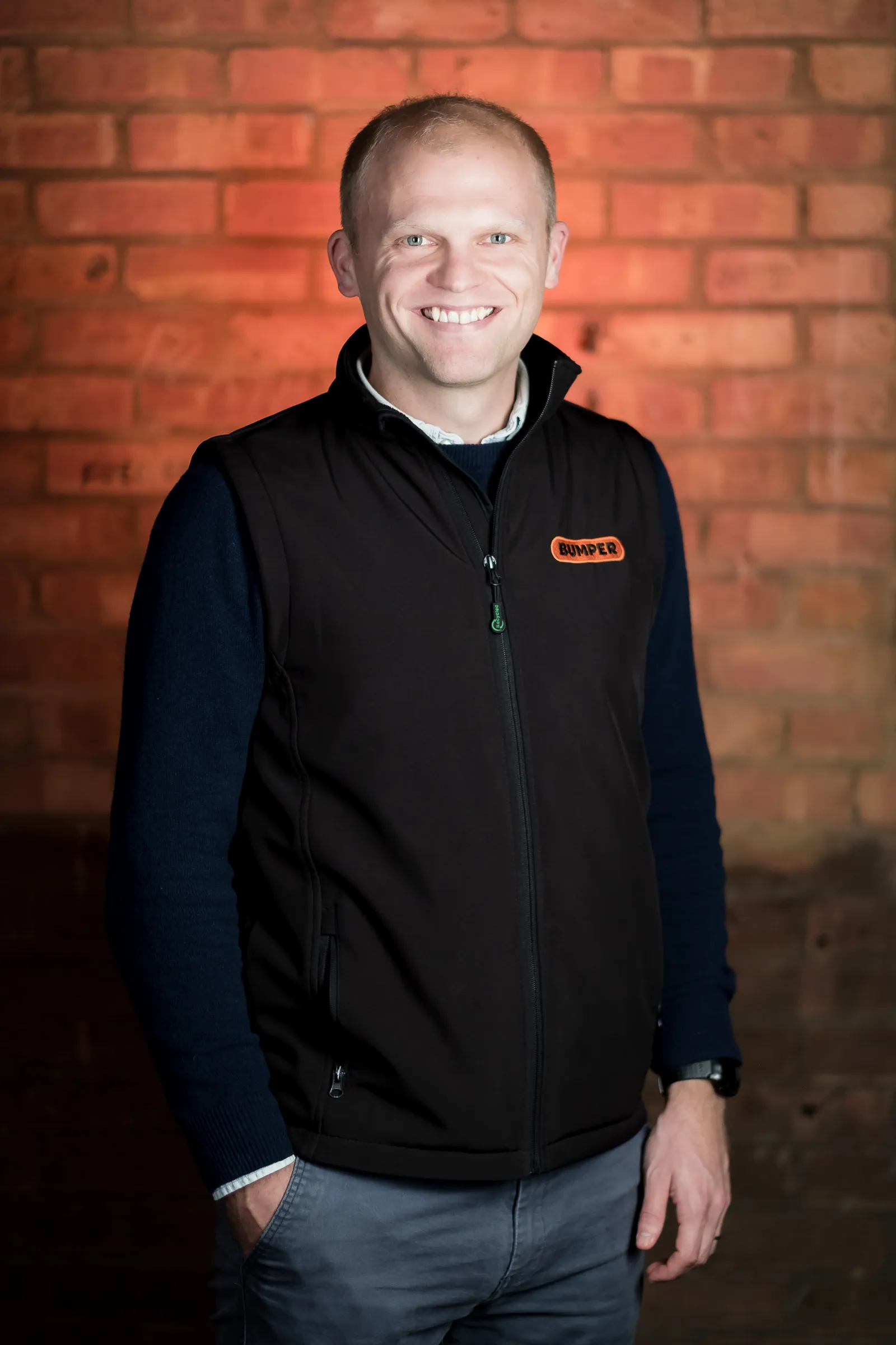 Bumper Team Photography - Three-quarter portrait, branded Bumper gilet, exposed brick backdrop