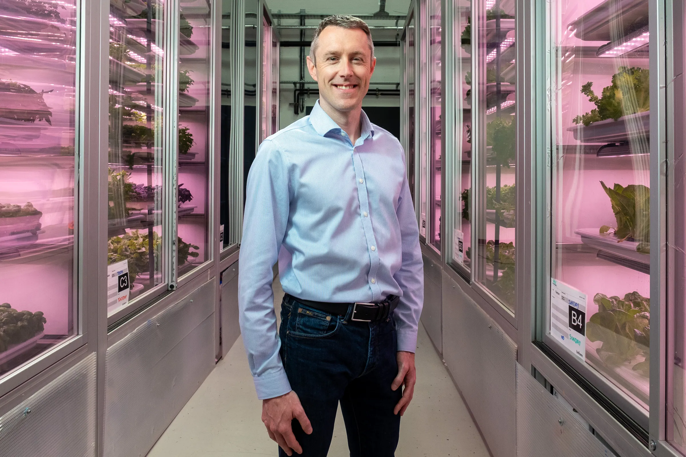Infarm London Team Photography - Team member in vertical farm corridor, blue shirt, pink grow-light backdrop
