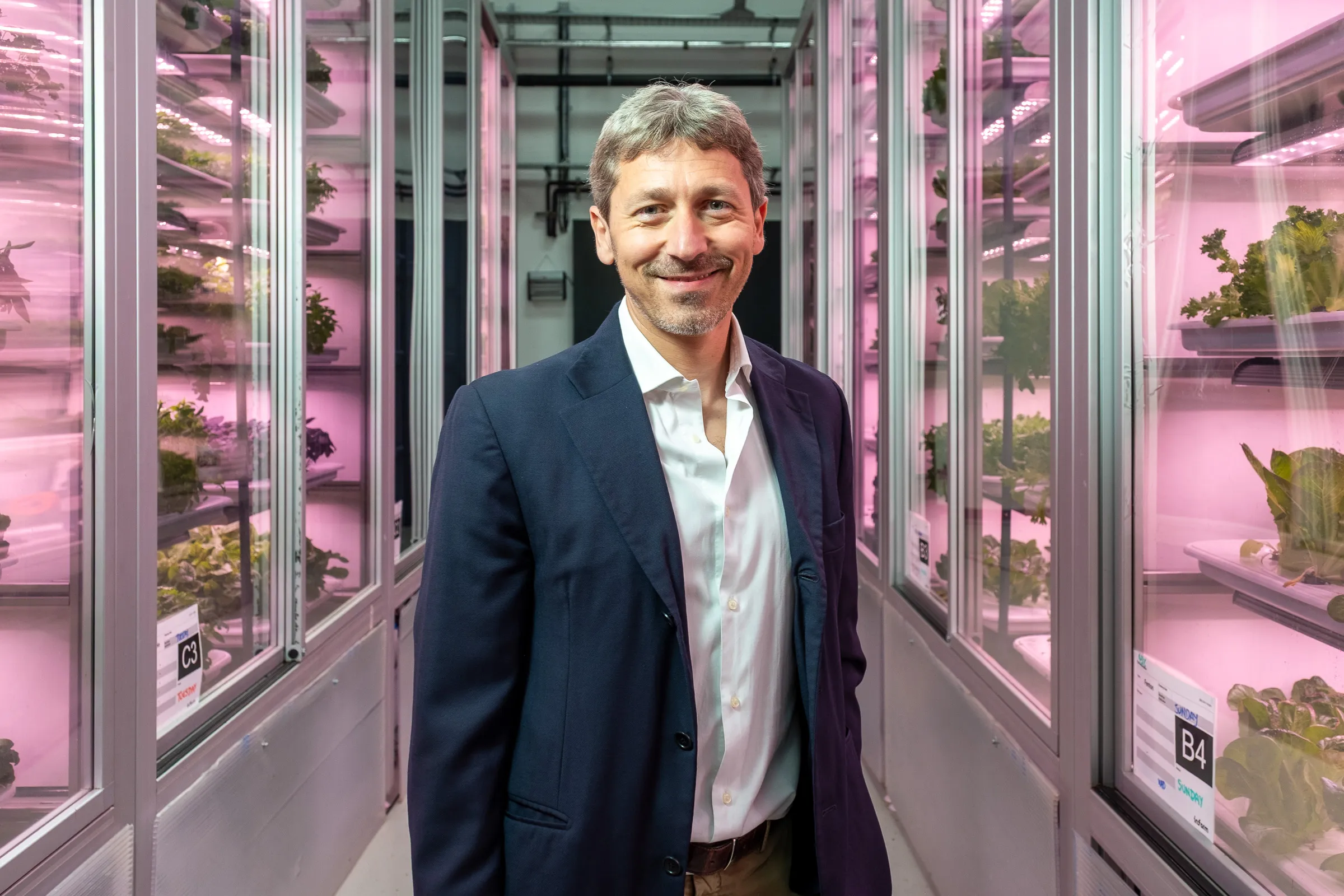 Infarm London Team Photography - Team member in vertical farm corridor, navy blazer, pink grow-light backdrop